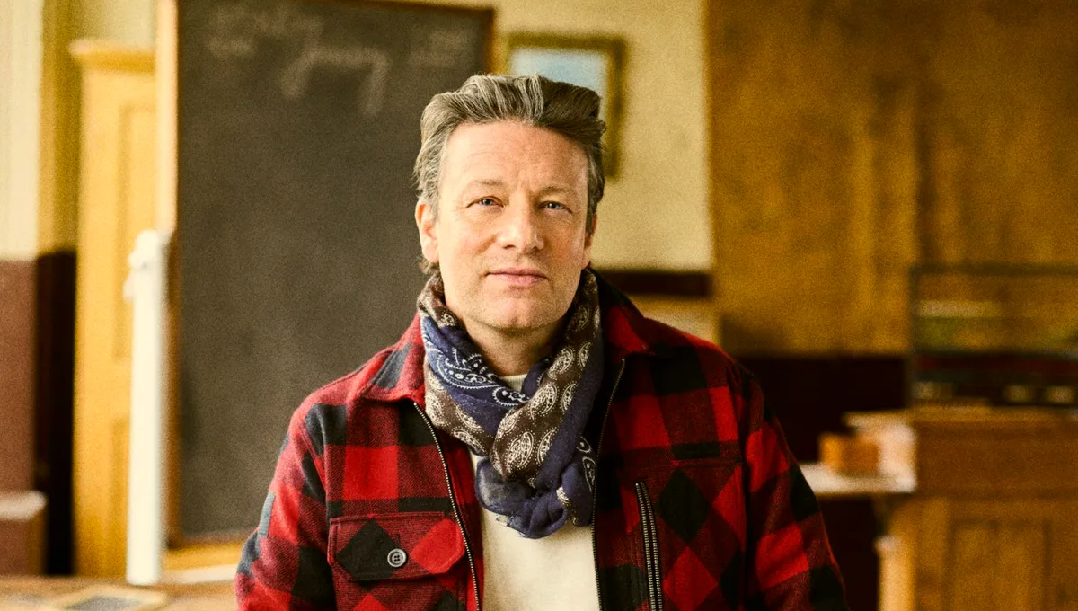 Jamie Oliver de camisa xadrez vermelha e preta em uma sala de aula.